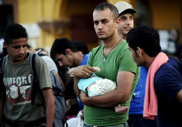 A Syrian man carries his 42-day-old son as they wait for the train at Gevgelija train station in Macedonia, near the border with Greece,  July 19, 2015. (Photo by Ognen Teofilovski/Reuters)