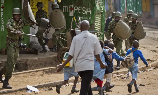 A policeman, left, yells at a man trying to lead schoolchildren to safety, because he was unknowingly about to walk into a hail of rocks thrown by protesters around the corner, as police firing tear gas engage protesters throwing rocks in the Kibera slum of Nairobi, Kenya Monday, May 23, 2016. (Photo by Ben Curtis/AP Photo)