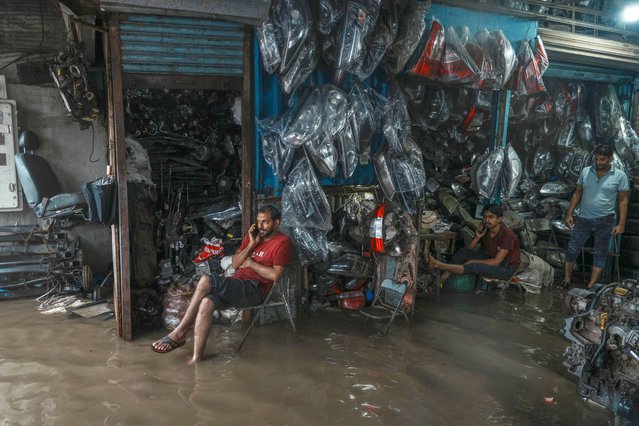 Auto repair employees watch water levels rise inside their shop during monsoon rains in Mumbai, India, July 25, 2024. (Photo by Rafiq Maqbool/AP Photo)