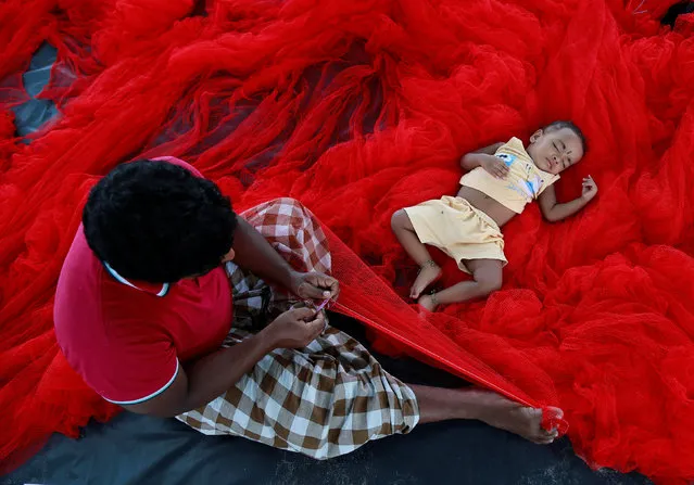 A fisherman stitches nets as his child sleeps beside him along the sea coast on the outskirts of Kochi, India May 23, 2017. (Photo by Sivaram V/Reuters)