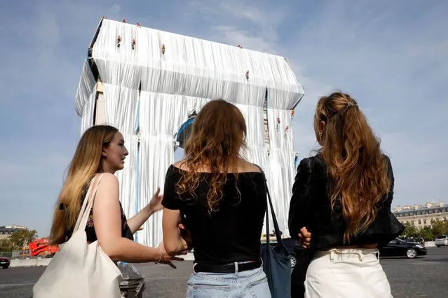 Bystanders look on as workers arrange silver blue fabric, part of the process of wrapping L'Arc de Triomphe in Paris on September 13, 2021, designed by the late artist Christo. Work has begun on wrapping the Arc de Triomphe in Paris in silvery-blue fabric as a posthumous tribute to the artist Christo, who had dreamt of the project for decades. Bulgarian-born Christo, a longtime Paris resident, had plans for sheathing the imposing war memorial at the top of the Champs-Elysees while renting an apartment near it in the 1960s (Photo by Geoffroy Van der Hasselt/AFP Photo)