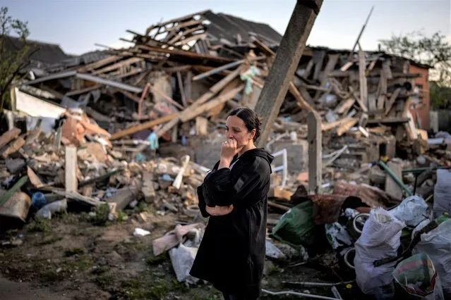 Anna Shevchenko, 35, reacts next to her home in Irpin, near Kyiv, Tuesday, May 3, 2022. The house, built by Shevchenko's grandparents, was nearly completely destroyed by bombing in late March during the Russian invasion of Ukraine. In her beloved flowerbed, some roses, lilies, peonies and daffodils survived. “It is new life. So I tried to save my flowers”, she said. (Photo by Emilio Morenatti/AP Photo)