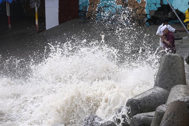 A man, right, performs rituals as waves hit the shore during high tide on the Arabian Sea coast in Mumbai, India, Wednesday, June 14, 2023. With Cyclone Biparjoy expected to make landfall Thursday evening, coastal regions of India and Pakistan are on high alert. (Photo by Rajanish Kakade/AP Photo)