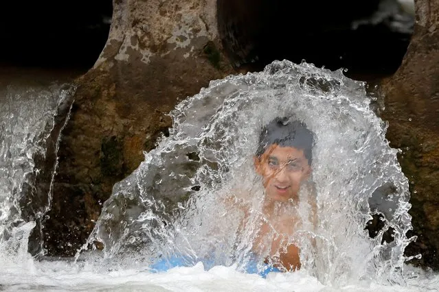 A boy bathes in a stream of water during a hot and humid weather in Peshawar, Pakistan, May 9, 2022. (Photo by Fayaz Aziz/Reuters)