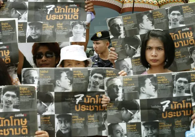 A Thai police officer (C) keeps watch as Thai supporters and friends of pro-democracy students display posters showing pictures of the seven members of the New Democracy Movement, arrested for violating the Referendum Act, outside of the Military Court in Bangkok, Thailand, 05 July 2016. Seven pro-democracy students activists, most of whom are members of the New Democracy Movement, were arrested on 23 June 2016 for allegedly for violating the Referendum Act by distributing leaflets urging a no vote on the scheduled on 07 August 2016 constitutional referendum. (Photo by Narong Sangnak/EPA)