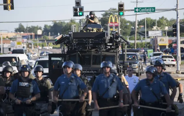 Riot police stand guard as demonstrators protest the shooting death of teenager Michael Brown in Ferguson, Missouri August 13, 2014. Police in Ferguson fired several rounds of tear gas to disperse protesters late on Wednesday, on the fourth night of demonstrations over the fatal shooting last weekend of an unarmed black teenager Brown, 18, by a police officer on Saturday after what police said was a struggle with a gun in a police car. (Photo by Mario Anzuoni/Reuters)