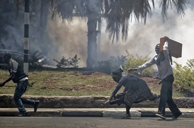 A passerby stumbles to the ground as she and opposition supporters, protesting over the upcoming elections, run for safety amid a cloud of tear gas fired by riot police in downtown Nairobi, Kenya Monday, October 16, 2017. Two international human rights groups said Monday that Kenya's police in August attacked opposition supporters killing dozens and injuring scores following demonstrations protesting President Uhuru Kenyatta's subsequently annulled re-election. (Photo by Ben Curtis/AP Photo)