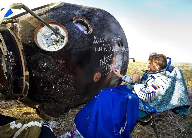 Russian cosmonaut Gennady Padalka signs an autograph on the Soyuz capsule after landing near the town of Arkalyk in northern Kazakhstan, on September 17, 2012. The capsule returned a trio of astronauts from a four-month stint on the International Space Station. (Photo by Shamil Zhumatov/Pool)