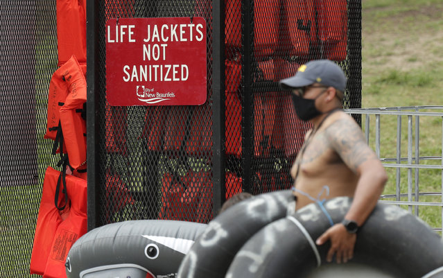 A tuber, wearing a mask to protect against the spread of COVID-19, passes a rack of life jackets as he prepares to float the Comal River, Thursday, June 25, 2020, in New Braunfels, Texas. Texas Gov. Greg Abbott said Wednesday that the state is facing a “massive outbreak” in the coronavirus pandemic and that some new local restrictions may be needed to protect hospital space for new patients. (Photo by Eric Gay/AP Photo)