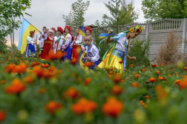 Children in traditional Ukrainian clothing run through a field after recording an online video message for the country's upcoming Independence Day on Aug. 24 at a community center in Andriivka, Donetsk region, eastern Ukraine, Friday, August 19, 2022. (Photo by David Goldman/AP Photo)
