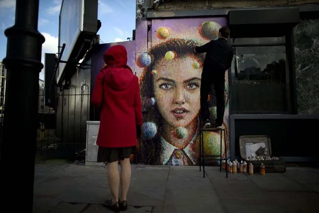 A passerby watches Australian artist James Cochran, also known as Jimmy C, put finishing touches to his spray painted 3D piece “Girl with Spheres in 3D” on the outside wall of a cafe in east London, November 22, 2012. The effects of the 3D painting can only be seen when the viewer looks through a pair of 3D glasses, which the cafe will keep a stock of to lend to people. (Photo by Matt Dunham/Associated Press)