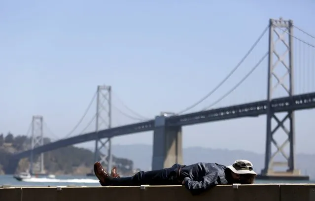 A man covers his face with a hat as he lays in the sun near the San Francisco Oakland Bay Bridge in San Francisco, California, August 31, 2015. (Photo by Robert Galbraith/Reuters)
