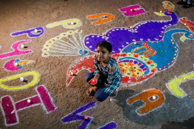 A girl poses with a rangoli, mural made out of coloured powders, outside her home during Diwali, the Hindu festival of lights, in Karachi, Pakistan on October 24, 2022. (Photo by Akhtar Soomro/Reuters)