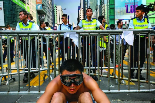 A protester sits front of barriers against police officers at a main street in Mong Kok district in Hong Kong Friday, October 17, 2014. Riot police cleared an offshoot Hong Kong pro-democracy protest zone in a dawn raid on Friday, taking down barricades, tents and canopies that have blocked key streets for more than two weeks, but leaving the city's main thoroughfare still in the hands of the activists. (Photo by Vincent Yu/AP Photo)