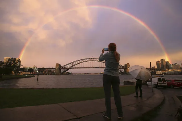 A woman takes a photograph as a rainbow forms over the Harbour Bridge on a wet day in Sydney Wednesday, June 17, 2015. (Photo by Rick Rycroft/AP Photo)