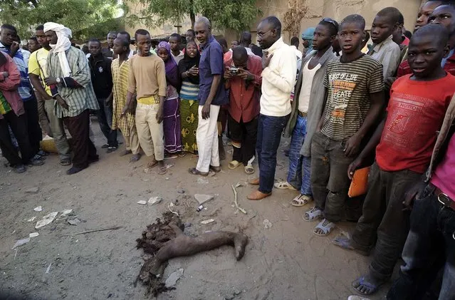 Malian people stand by the remain of a suicide bomber who blew himself up the day before in front of a police station in the northern Mali's largest city of Gao, on February 11, 2013. France bombed an Islamist hideout today in Gao, where troops rattled by guerrilla attacks intensified a security lock-down as the French-led campaign against the extremists entered its second month. (Photo by Pascal Guyot/AFP Photo)