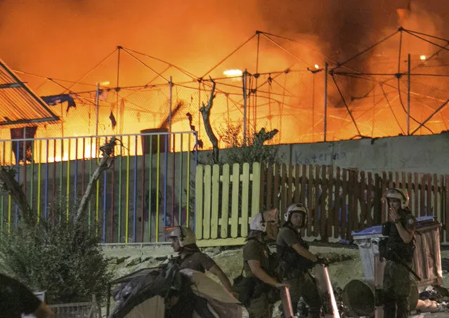 Riot police stand guard as a large fire burns inside the Moria refugee camp on the northeastern Greek island of Lesbos, late Monday, September 19. 2016. Greek police say a large fire swept through the big camp for refugees and other migrants on the eastern Aegean island of Lesbos, forcing its evacuation. None of the more than 4,000 people in the Moria camp was reported injured in Monday's blaze, which damaged tents and prefabricated housing units. (Photo by Michael Schwarz/AP Photo)