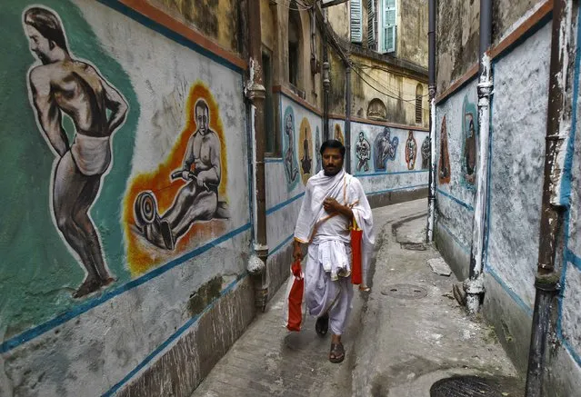 A Hindu priest walks in an alley with painted walls depicting a traditional Indian wrestling training centre called “Akhaara”, in Kolkata November 17, 2014. (Photo by Rupak De Chowdhuri/Reuters)