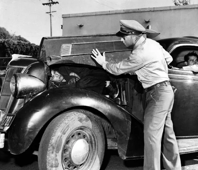 U.S. Border Patrol officer Richard McCown shows how he found Felipe Ramirez Perez, a 6-foot illegal Mexican immigrant, curled up on the engine beneath the hood of this automobile, at the U.S.-Mexican border at San Diego, Calif., March 15, 1954. Perez is held for illegal entry, awaiting deportation, and Felix Mercado Gutierrez, the driver of the car, is charged with attempt to smuggle Perez into the United States. (Photo by AP Photo)