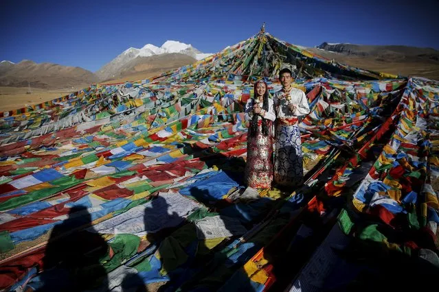 Jing Li (L) and her husband Ke Xu wear Tibetan traditional costumes as they pose for their wedding photos in front of Tibetan prayer flags at the Nianqing Tanggula mountain pass in the Tibet Autonomous Region, China November 18, 2015. Ke, 23, and Jing,22, both from Shiyan in northwestern Hubei province live in Tibet for three year. The couple married last month. (Photo by Damir Sagolj/Reuters)