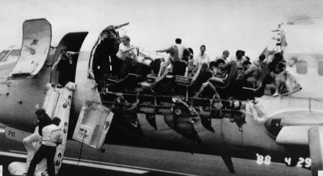 Co-pilot Mimi Tompkins, standing in doorway, helps a man slide down a chute of a heavily damaged Aloha Airlines jet shortly after landing on April 30, 1988. Pilot Robert Schornstheimer, at front of damaged section, looks on. (Photo by AP Photo)