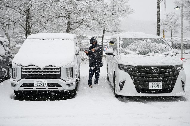 A man clears snow from cars in Chitose, in Japan's northern Hokkaido prefecture on December 8, 2025. (Photo by Greg Baker/AFP Photo)