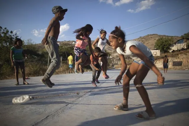Children jump a rope as they play at a court close to the Pavia garbage dump in Barquisimeto, Venezuela, Wednesday, March. 3, 2021. The enormous Pavia garbage dump, where all of the city's solid waste is deposited, serves as a source of income for poor people who work recycling whatever they can find in the mountains of refuse. (Photo by Ariana Cubillos/AP Photo)