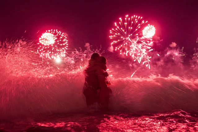 A wave crashes on two girls hugging as they usher in the new year, while fireworks explode over Copacabana beach, during New Year celebrations in Rio de Janeiro, Brazil, Thursday, January 1, 2015. (Photo by Felipe Dana/AP Photo)