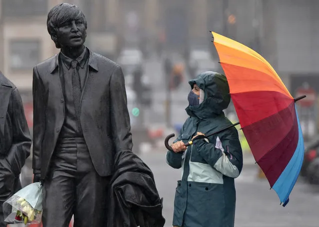 A youth wearing a face mask looks up at statue of John Lennon, part of a larger statue of The Beatles in Liverpool, England, Monday October 12, 2020, as Prime Minister Boris Johnson prepares to lay out a new three-tier alert system for England. The Liverpool City Region is expected to face the tightest restrictions under the new system, which will classify regions as being on “medium”, “high” or “very high” alert. (Photo by Jon Super/AP Photo)