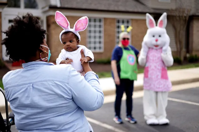 A woman holds her baby as they approach a person dressed as an Easter Bunny during a Bunny Drive-Thru event outside Kingstowne Snyder Fitness Center March 27, 2021 in Alexandria, Virginia. Kingstowne Residential Owners Corporation held the community event instead of the usual annual egg hunt for neighborhood children to celebrate Easter in a safer environment under the COVID-19 pandemic. (Photo by Alex Wong/Getty Images)