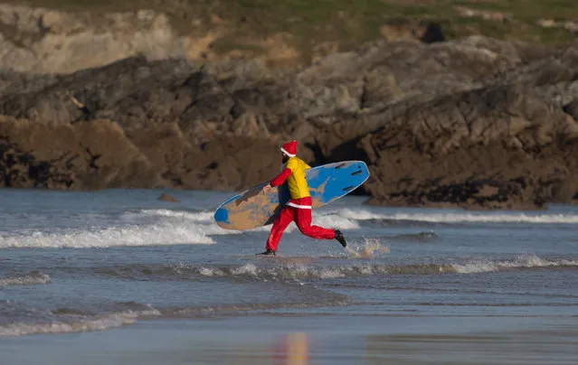 A surfer dressed as Santa runs to sea as he competes in a heat during the annual Surfing Santa as part of the Santa Run and Surf 2016 at Fistral Beach in Newquay on December 4, 2016 in Cornwall, England. (Photo by Matt Cardy/Getty Images)