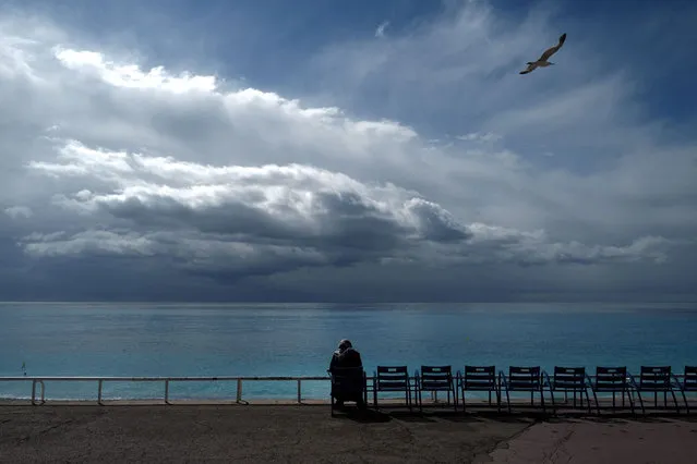 An inhabitant sits on one of the blue chairs facing the Mediterranean sea, on the “Promenade des Anglais”, in the French riviera city of Nice, on April 7, 2021 while the sky is clouding over. (Photo by Valery Hache/AFP Photo)