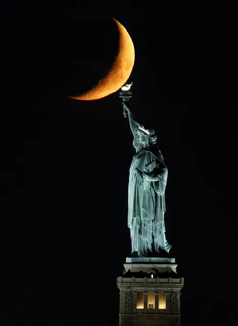 A 22 percent illuminated waxing crescent moon sets behind the Statue of Liberty on September 19, 2023, in New York City. (Photo by Gary Hershorn/Getty Images)