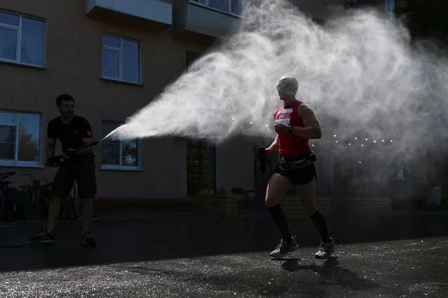 A participant of the half-marathon race is sprayed with water during hot weather in Omsk, Russia on May 30, 2021. (Photo by Alexey Malgavko/Reuters)