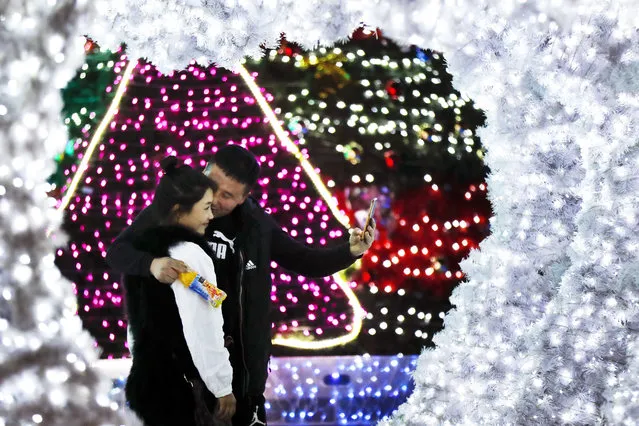A man kisses his partner as they take a selfie near light installation decorated for the Christmas season outside an office building in Beijing, Thursday, December 1, 2016. Although Christmas is not traditionally celebrated in China, some office buildings and shopping malls welcome the festival with colorful decorations. (Photo by Andy Wong/AP Photo)