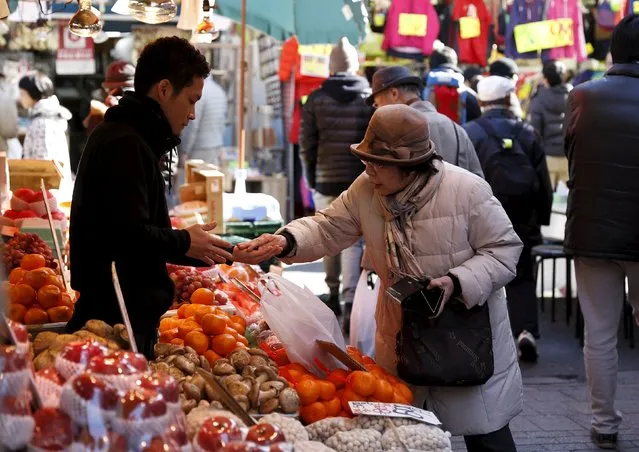 A woman pays money as she buys fruits outside a vegetable store at Ameyoko shopping district in Tokyo, Japan, January 27, 2016. (Photo by Yuya Shino/Reuters)