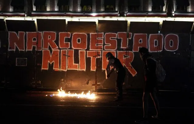 Demonstrators start a fire at the foot of the barrier protecting the National Palace during a march to commemorate the 9th anniversary of the disappearance of 43 missing Ayotzinapa university students, in Mexico City, Tuesday, September 26, 2023. The graffiti on the barrier reads “Military Narcostate” in Spanish. (Photo by Marco Ugarte/AP Photo)
