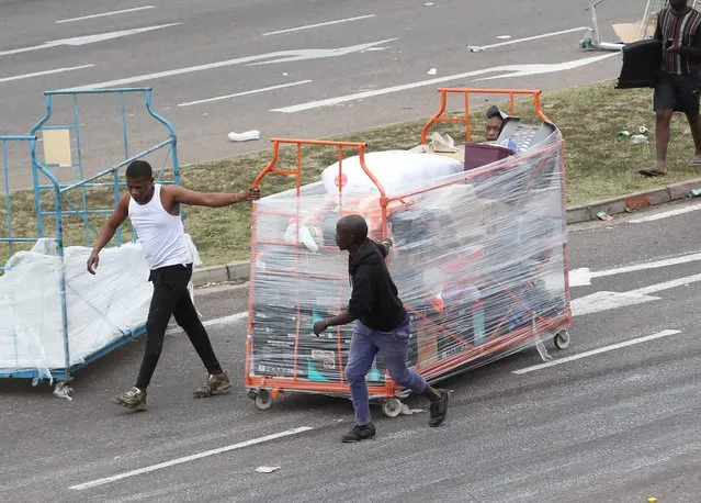People make their way with good on a trolley from a store in Durban, South Africa, Tuesday July 13, 2021, as ongoing looting and violence continues. (Photo by AP Photo/Stringer)