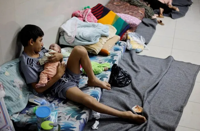 A displaced Palestinian boy, who fled with his family from their house amid Israeli strikes, looks after his twin siblings as they take shelter at Nasser hospital in Khan Younis in the southern Gaza Strip on October 29, 2023. (Photo by Mohammed Salem/Reuters)