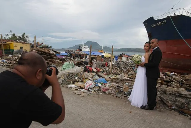 A photographer shoots Filipino groom Earvin Nierva and his bride Riza as they pose for their wedding pictures beside damaged homes and a ship that was washed ashore when Typhoon Haiyan hit Tacloban city, central Philippines on Saturday, December 7, 2013. The newly-wed couple decided to have the photo shoot at the area to symbolize that they can overcome tragedy and to urge residents to “stand up and rise again”. (Photo by Aaron Favila/AP Photo)