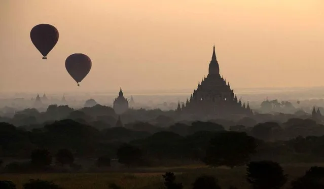 Hot air balloons with tourists fly over ancient pagodas and temples in Bagan, Myanmar, Saturday, December 21, 2013. Bagan, one of the richest archaeological sites and tourist attractions in Myanmar has over 2,000 preserved temples and pagodas built between 11th-13th century. (Photo by Gemunu Amarasinghe/AP Photo)