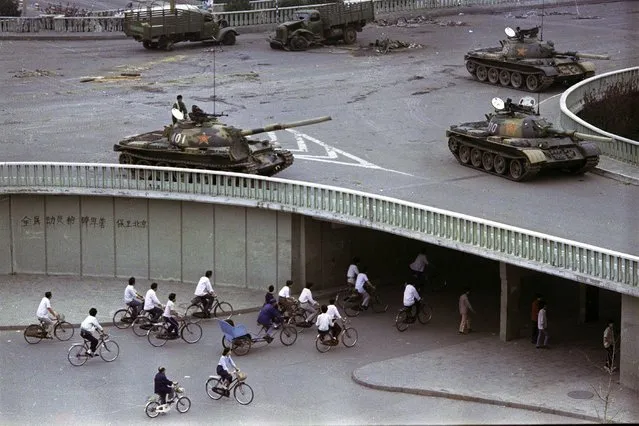 In this June 6, 1989, file photo, bicycling commuters, sparse in numbers, pass through a tunnel as above on the overpass military tanks are positioned in Beijing, two days after the Tiananmen Square massacre. Hong Kong’s second ban on an annual vigil for victims of the bloody June 4, 1989 crackdown on Beijing’s Tiananmen Square protest movement and the closure of a museum dedicated to the event may be a further sign that the ruling Communist Party is extending its efforts to erase the event from the collective consciousness of Chinese people. The slogan on the wall at left reads: “Strike down martial law”. (Photo by Vincent Yu/AP Photo/File)