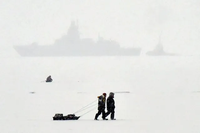 Fishermen walk on the ice-covered Gulf of Finland in front of a warship during a snowfall in Saint Petersburg on December 26, 2023. (Photo by Olga Maltseva/AFP Photo)