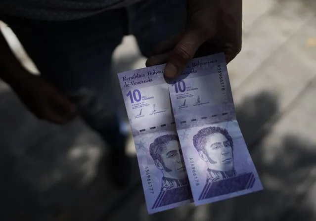 A man shows a new 10 Bolivar bank note after withdrawing it from a cash machine in Caracas, Venezuela, Friday, October 1, 2021. A new currency with six fewer zeros debuts Friday in Venezuela, whose currency has been made nearly worthless by years of the world's worst inflation. The new currency tops out at 100 bolivars, a little less than $25 until inflation starts to eat away at that as well. (Photo by Ariana Cubillos/AP Photo)