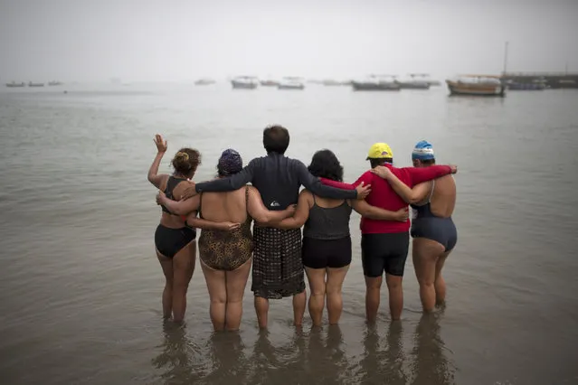 In this April 9, 2015 photo, a therapy group who have become friends pray on Fishermen's Beach before taking a therapeutic swim in the Pacific Ocean in Lima, Peru. “The sea is the pharmacy of humanity”, said natural therapy promoter Jose Cusquisiban, who organizes therapy groups. “It has many minerals, vitamins”. (Photo by Rodrigo Abd/AP Photo)