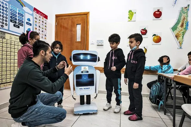 Palestinian teacher Hassan al-Rozy (L) gives a science class to students in his classroom while aided by a locally-made educational robot, at a private school in Gaza City on November 30, 2021. (Photo by Mahmud Hams/AFP Photo)