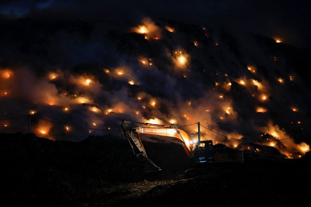 An excavator tries to contain the fire as smoke rises from burning garbage following a fire at Ghazipur landfill site in New Delhi, India on April 22, 2024. (Photo by Adnan Abidi/Reuters)