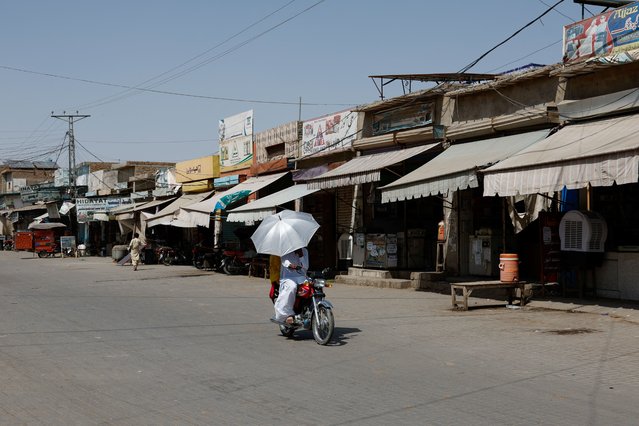 A couple rides on a motorbike carrying an umbrella to avoid sunlight, along a deserted market during a hot summer day as the heatwave continues in Jacobabad, Pakistan on May 26, 2024. (Photo by Akhtar Soomro/Reuters)