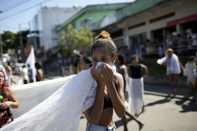 A woman covers her face with a white table cloth, used as a flag to call for peace, against pepper spray launched by police during a protest against police and gang conflicts that put residents in the crossfire at the Complexo de Alemao slum in Rio de Janeiro, Brazil, Tuesday, April 25, 2017. Residents are protesting after a youth died in a shootout early Tuesday. (Photo by Silvia Izquierdo/AP Photo)