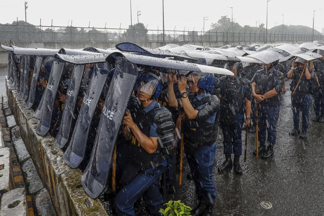 Police personnel use shields as cover during rainfall along the main road leading to the House of Representatives ahead of  the third State of the Nation Address by Philippine President Ferdinand Marcos Jr. in Quezon City, Philippines, Monday, July 22, 2024. (Photo by Mark Cristino/AP Photo)